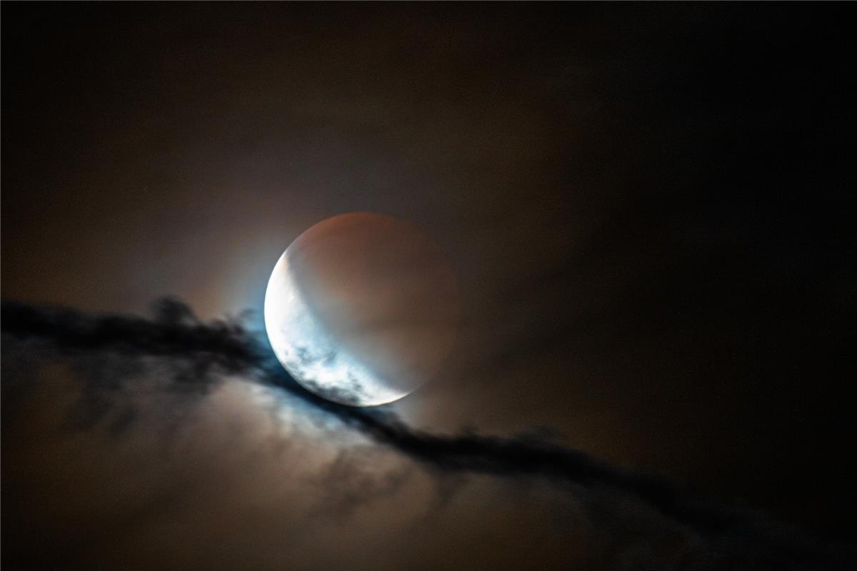 Der Blutmond tritt langsam aus dem Erdschatten und ist gebettet auf einem Konden...