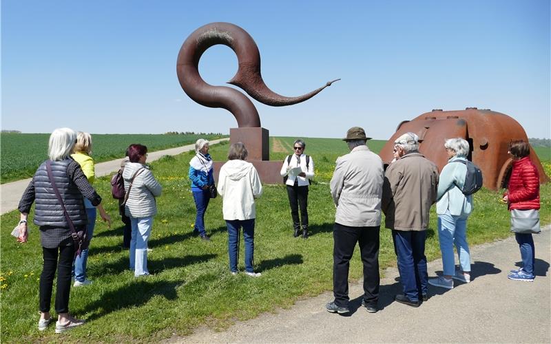 Der Spaziergang führte auch zum Wegweiser des Skulpturengartens von Künstler Lutz Ackermann, wo Gabi Weber-Urban (Mitte) die „Kriegsandenken“ von Kurt Tucholsky rezitierte. GB-Foto: Stadler