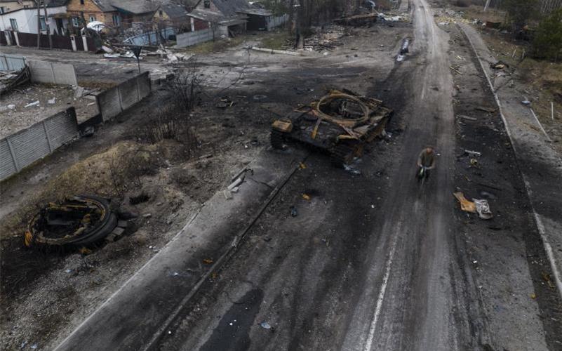 Ein Fahrradfaher fährt auf einer Straße in Kiew an einem zerstörten russischen Panzer vorbei. Foto: Rodrigo Abd/AP/dpa