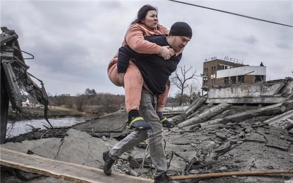 Ein Mann trägt eine Frau durch Trümmer. Sie sind auf der Flucht aus der ukrainischen Stadt Irpin. Foto: Oleksandr Ratushniak/AP/dpa