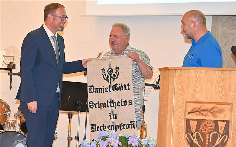 Ein originelles Geschenk für Daniel Gött (links). So wie früher Getreide- oder Obstsäcke beschriftet wurden, überreichten ihm Lothar Schneider (rechts), Vorstandssprecher des Liederkranzes, und Götz Zinser (Mitte ) von der Volkstanzgruppe im Namen der Vereine einen Wandbehang. Die Aufschrift: Daniel Gött, Schultheiss in Deckenpfronn 2009 – 2025. GB-Fotos: Reichert