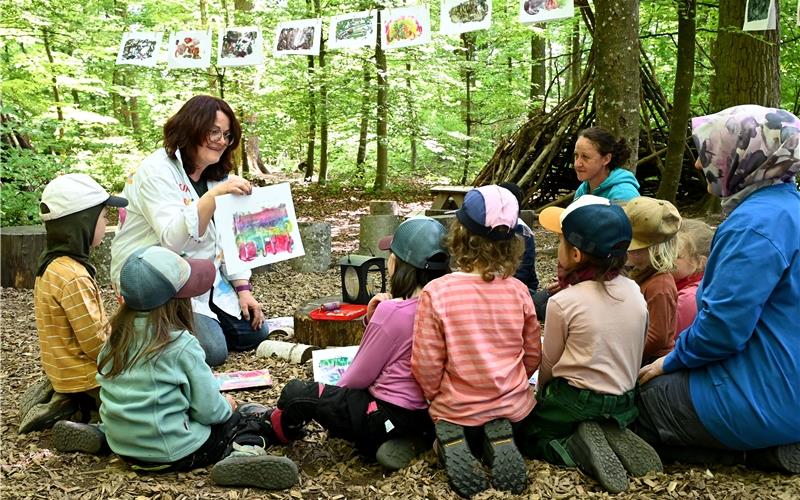 Künstlerin Elena Schmidt zeigt den Jungen und Mädchen des Nufringer Waldkindergartens „Wilde Füchse“ die Ergebnisse eines Kunstprojekts. An einer Wäscheleine zwischen Bäumen hängen einige Monotypien aus der ersten Projektphase.GB-Foto: Holom