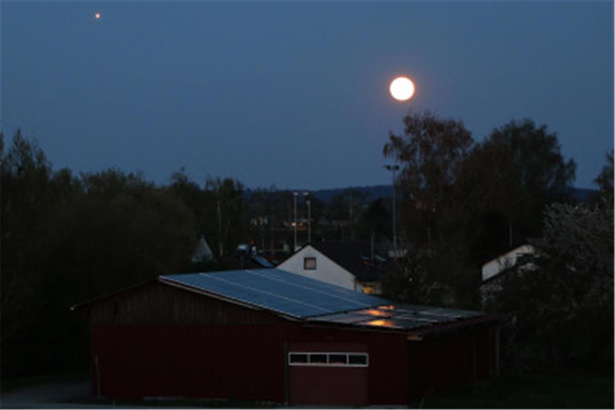 Über dem Ammerstadion in Gültstein steht der Vollmond und ein Flugzeug ist im An...