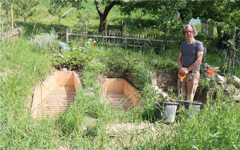 Zwei fertige Holzkonstruktionen für das Kunstprojekt „Internationaler Testfriedhof“ liegen bereits in der Erde im Garten unweit des Reustener „Bergcafés“. Die dritte Grube hebt Daniel Schürer derzeit aus. Wer mag, kann sich eine Weile hineinlegen. GB-Foto: Priotto